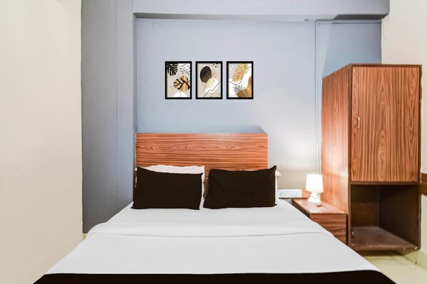 A hotel room with a bed, two black pillows, a wooden headboard, a nightstand with a lamp, and a wardrobe. - Deluxe Paradise Circle (Hyderabad)