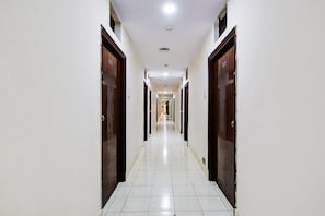 A long, narrow hallway with white tiled floors and wooden doors on both sides. - Deluxe Paradise Circle (Hyderabad)