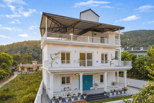 Un immeuble de deux étages doté d’un balcon, de plantes en pot et d’une porte bleue.