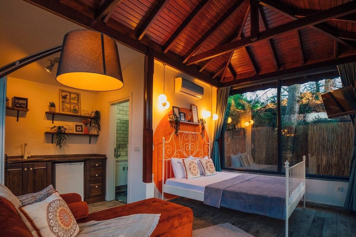 A cozy bedroom with a bed, a sofa, a desk, and a large window.