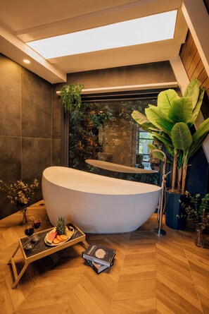 A modern bathroom with a freestanding bathtub, a wooden floor, a small table with a fruit platter and wine glasses, and a large plant. - Sapanca Fitos Bungalov (Sapanca)