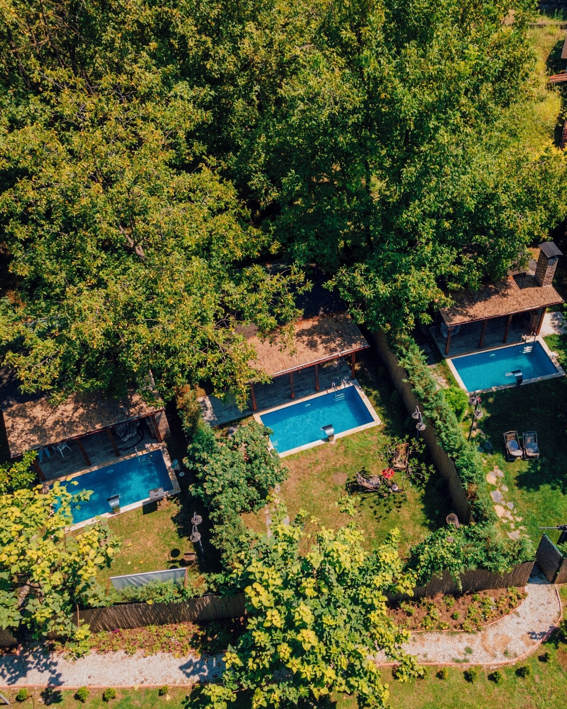 An aerial view of a property with three swimming pools surrounded by lush greenery and a thatched-roof structure.