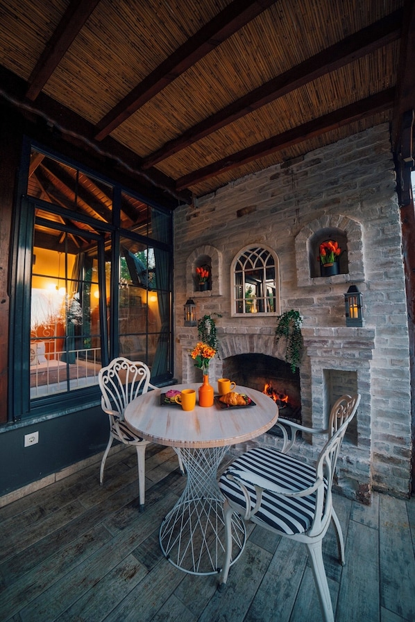 A stone fireplace with a round table and chairs, a wooden ceiling, and a view through a window. - Sapanca Fitos Bungalov (Sapanca)