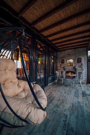 A cozy outdoor seating area with a hanging chair, a round table, and a fireplace. - Sapanca Fitos Bungalov (Sapanca)