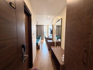 Habitació d'hotel amb terra de fusta, escriptori, cadira, llit, televisió i mirall.
