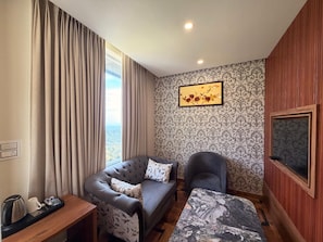 A hotel room with a sofa, armchair, and a bed with a marble headboard. - EL PINO (Dharamshala)