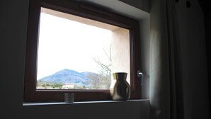 Ein Fenster mit Blick auf Berge, eine Vase auf dem Sims und eine Tür zur rechten Seite.