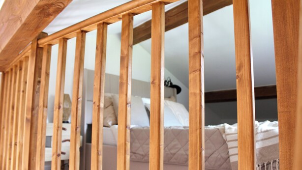 Eine Holzhandläufe einer Treppe führt zu einem Schlafzimmer mit Bett und Nachttisch.