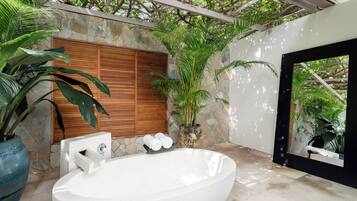 A spa area with a large freestanding bathtub, a wooden door, and a stone wall.
