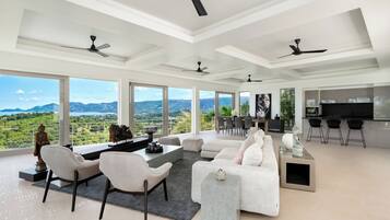 A spacious living area with a large window, ceiling fans, a dining area, and a kitchen.