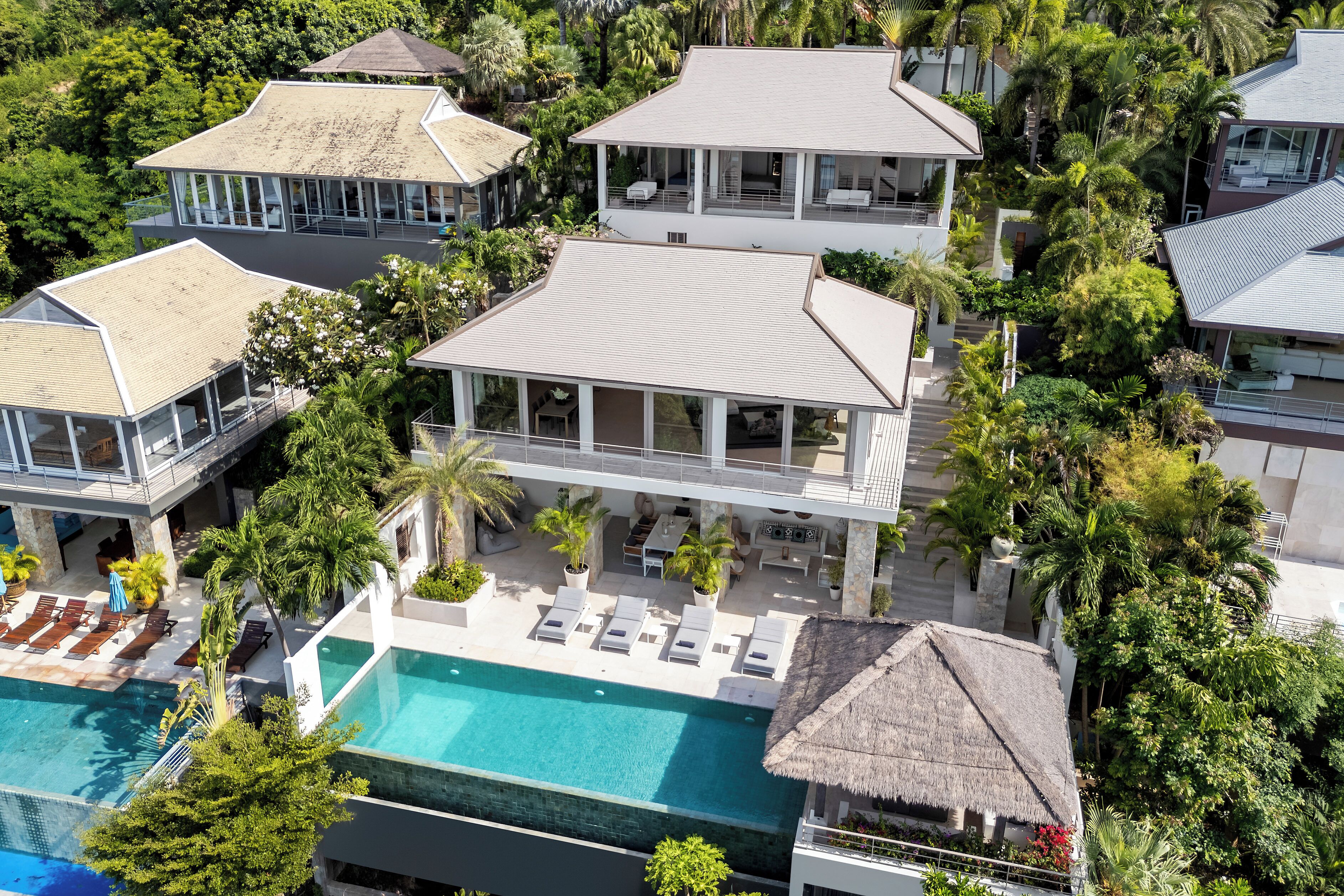 A multi-story resort with a swimming pool, lounge areas, and a thatched-roof structure.