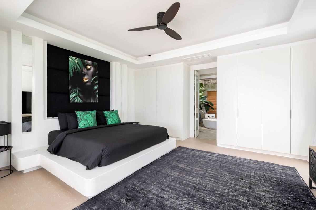 Une chambre moderne avec un grand lit, un ventilateur de plafond et une vue sur la salle de bain adjacente.