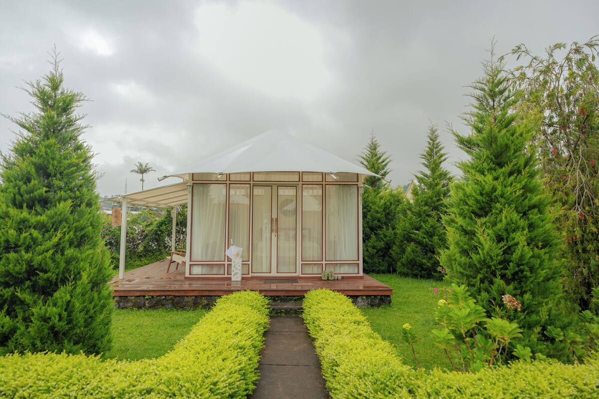 A gazebo-style structure with a glass enclosure, surrounded by lush greenery and a well-maintained garden.