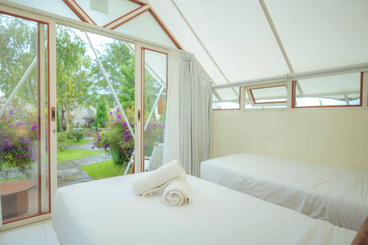 A room with two beds, a sliding glass door to a garden, and a white ceiling.