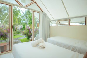 A room with two beds, a sliding glass door to a garden, and a white ceiling.