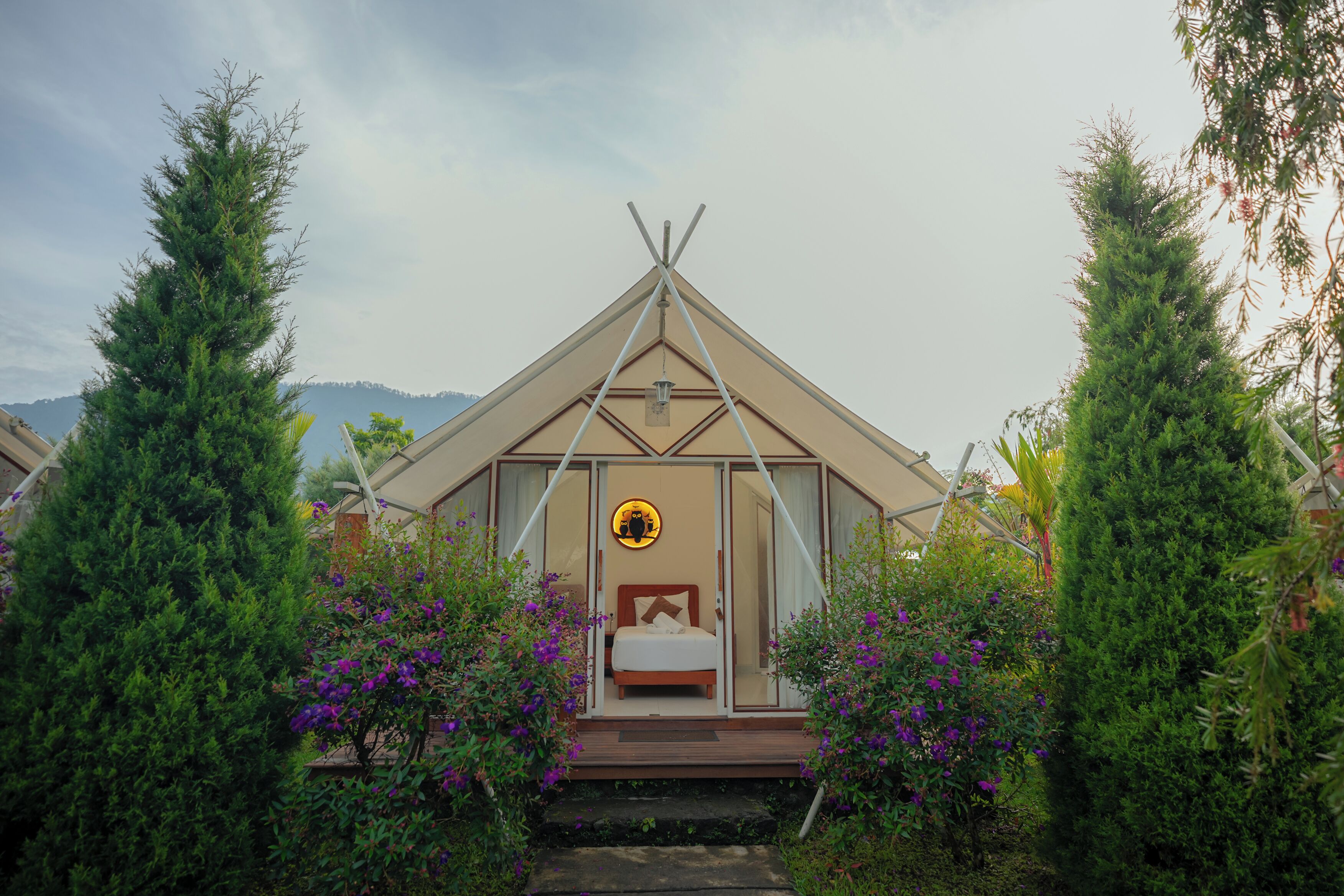 A cozy, triangular-roofed tent-style accommodation with a bed and a circular window.