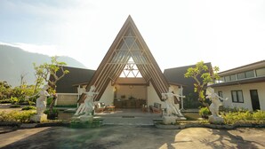 A triangular building with a central skylight, surrounded by statues and a garden. - Svargan Lakeside Glamping & Restaurant (Baturiti)