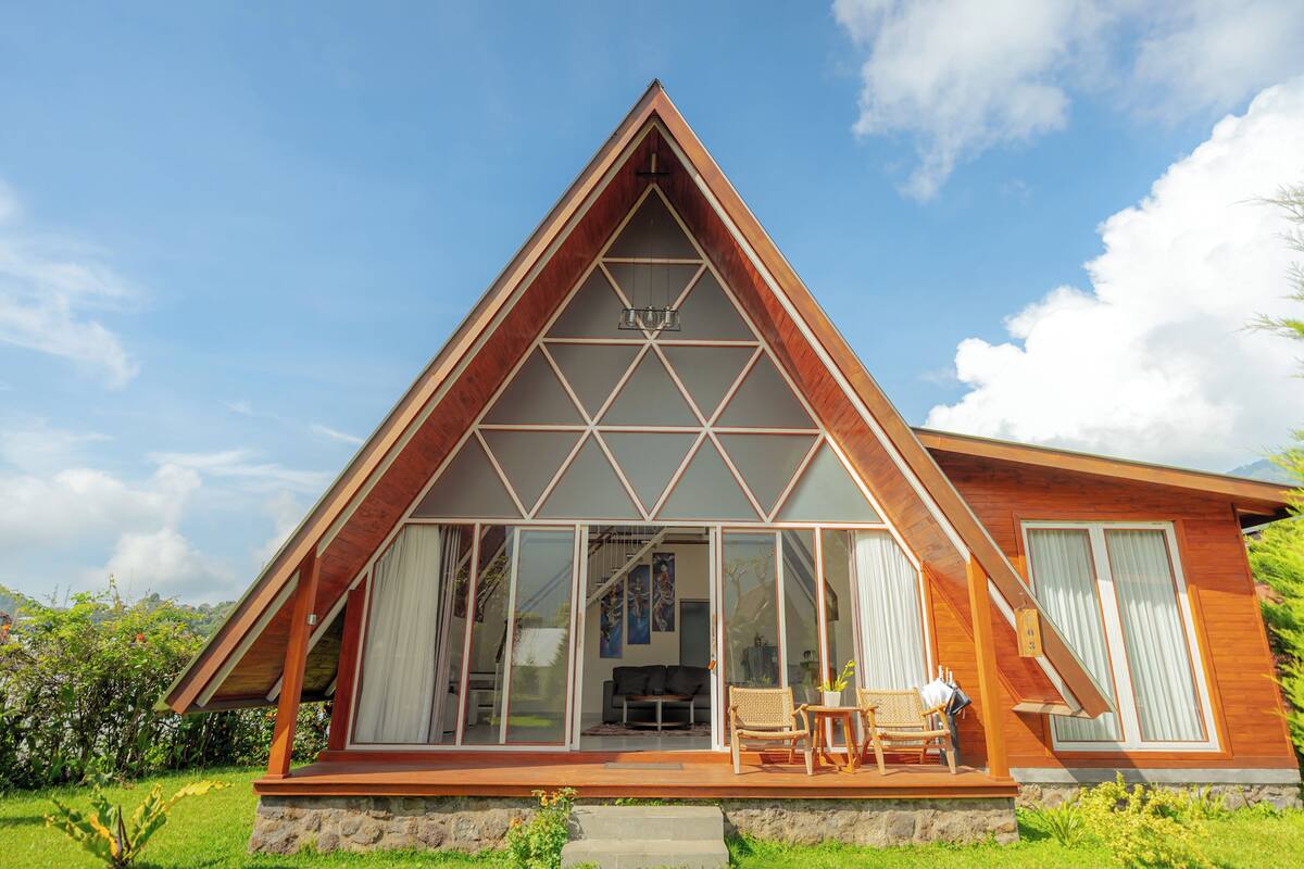 A modern house with a triangular roof, large glass windows, and a wooden deck.