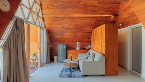 A modern living room with wooden ceiling, a sofa, a coffee table, and a small table with a vase. - Svargan Lakeside Glamping & Restaurant (Baturiti)