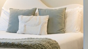 Una cama con cabecera blanca, dos almohadas, una manta blanca y una manta tejida verde.