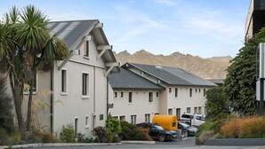 Un edificio residencial con varias unidades, un estacionamiento y montañas al fondo.