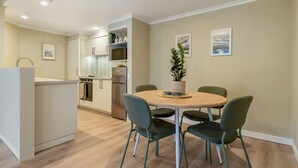 Una cocina moderna con armarios blancos, un comedor con una mesa redonda y cuatro sillas, y una pequeña planta en maceta sobre la mesa.