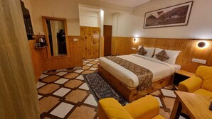 A hotel room with a bed, a wooden wardrobe, a mirror, a small table, and a yellow armchair. - Carom Inn (Manali)