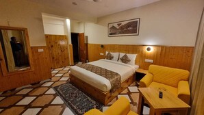 A bedroom with a bed, a yellow armchair, a small table, and a mirror. - Carom Inn (Manali)