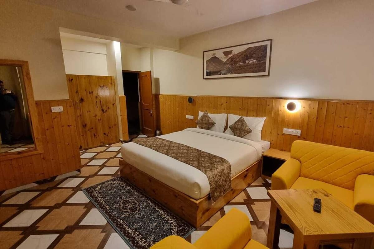A bedroom with a bed, a yellow armchair, a small table, and a mirror.