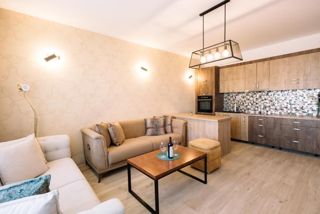 A modern living room with a sofa, coffee table, and a kitchen area with wooden cabinets and a tiled backsplash.