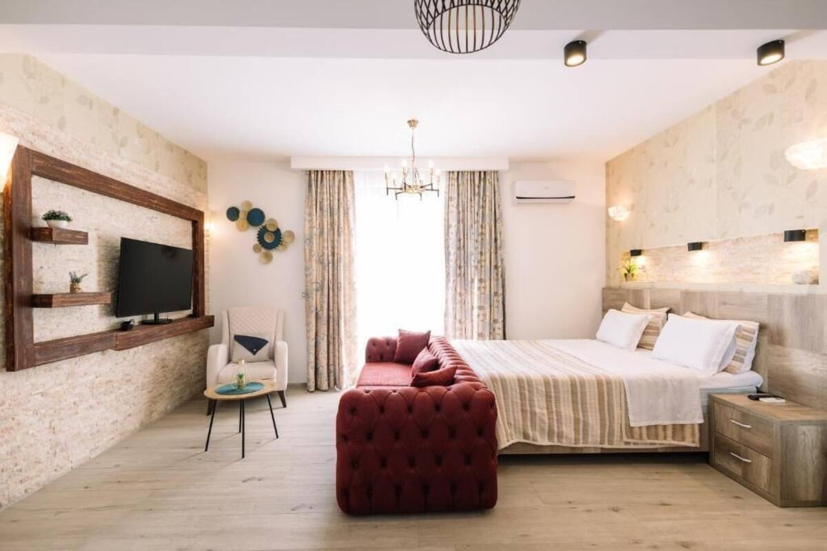 A bedroom with a bed, a TV mounted on the wall, a chair, and a red ottoman.