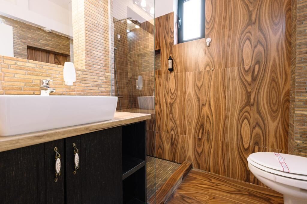 Un bany modern amb una paret de fusta, un lavabo blanc i un plat de dutxa amb envàs de vidre.