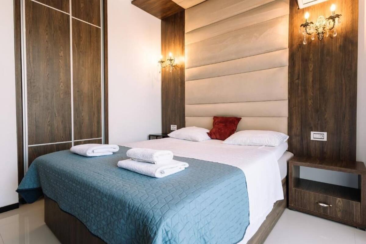 A hotel room with a large bed, two bedside tables, a nightstand, and a wall-mounted light fixture.