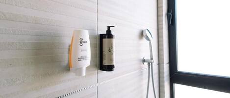 A bathroom with a white tiled wall, a hand soap dispenser, a shampoo bottle, and a showerhead.