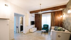 A living room with a sofa, a small round table, a TV mounted on the wall, and a wooden accent wall.