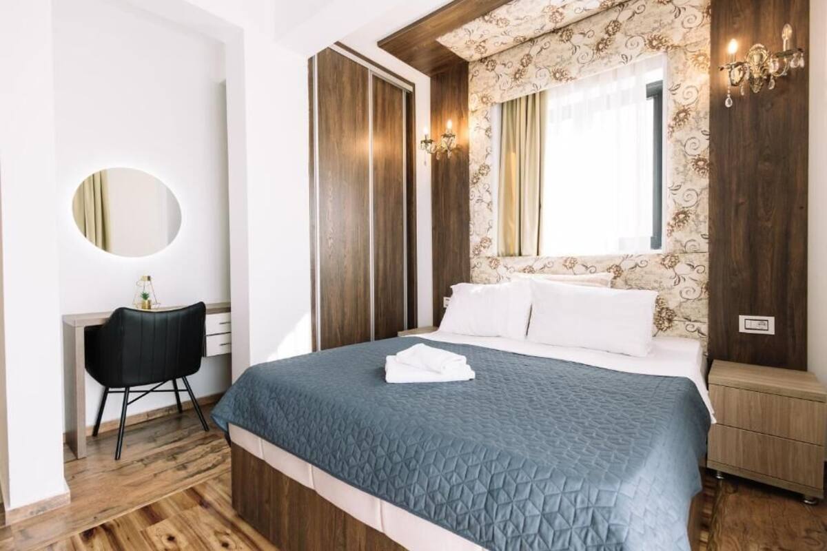 A hotel room with a bed, a desk, a chair, a mirror, and a window with curtains.