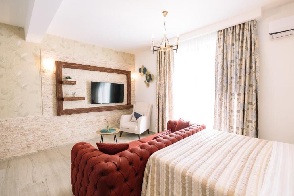 Une chambre d’hôtel avec un lit, un téléviseur fixé au mur, une petite table d’appoint, une chaise et une grande fenêtre avec des rideaux.