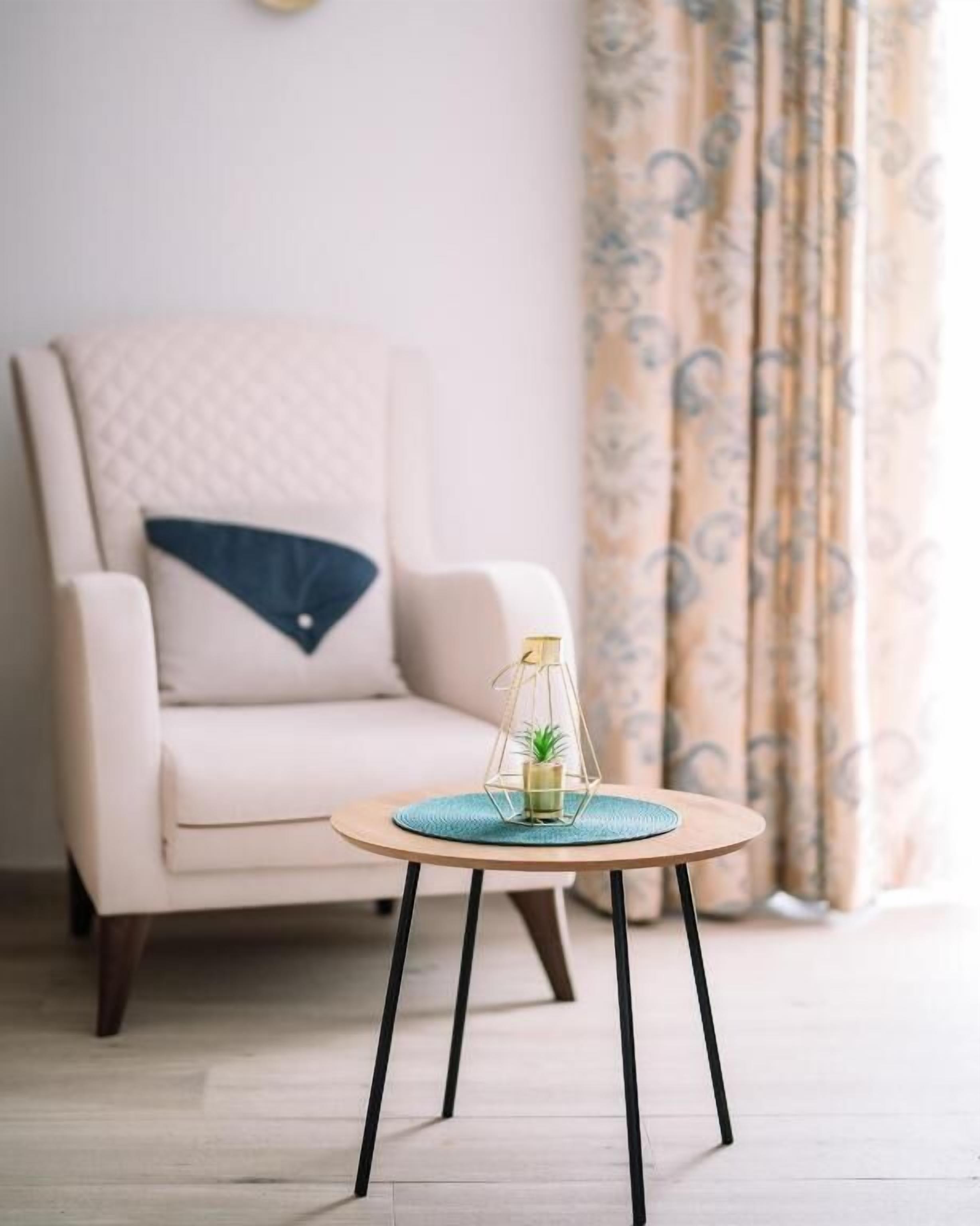 A room with a light-colored sofa, a small round table with a plant, and patterned curtains.