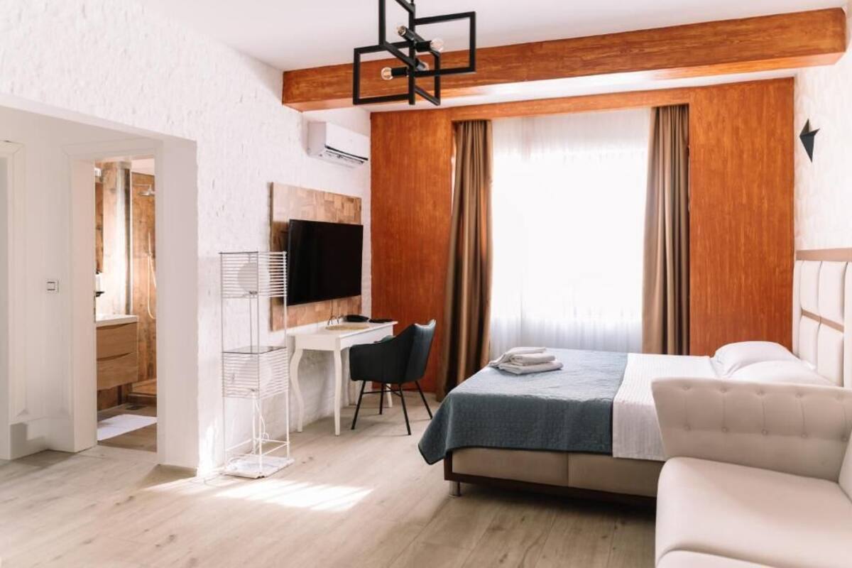 A modern hotel room with a bed, a desk, a chair, a TV, and a wardrobe.