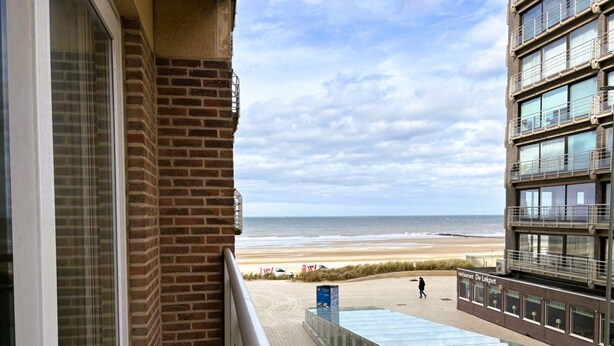 A balcony with a view of the beach, a glass railing, and a building with multiple windows. - Modern Stay With Balcony & Seaview (Middelkerke)
