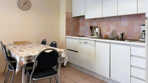 A compact kitchen with white cabinets, a dining table with chairs, a clock, and basic kitchen appliances. - Modern Stay With Balcony & Seaview (Middelkerke)