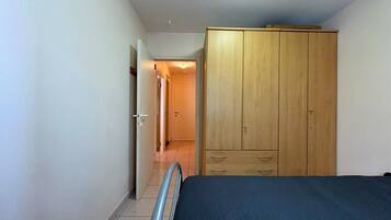 A bedroom with a bed, wooden wardrobe, and a door leading to another room.