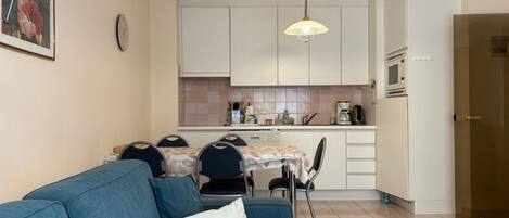 A compact living space with a sofa, dining table, chairs, a kitchenette, and a ceiling light fixture.