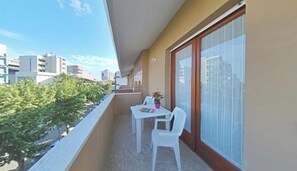 Ein Balkon mit weißem Tisch und Stühlen, einem Blumentopf und Blick auf die Stadt.