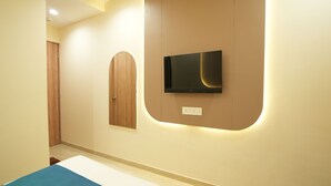 A bedroom with a bed, a television mounted on the wall, and a wooden door. - Privilon Hotel Prahladnagar (Ahmedabad)