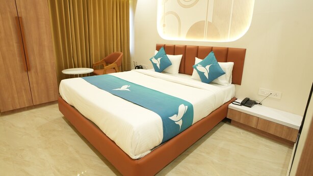 A modern hotel room with a large bed, a bedside table, a chair, and a curtain. - Privilon Hotel Prahladnagar (Ahmedabad)