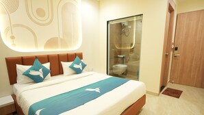 A modern hotel room with a large bed, a glass-enclosed shower, and a wooden door. - Privilon Hotel Prahladnagar (Ahmedabad)