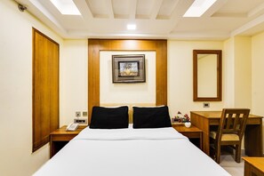 A hotel room with a bed, a desk, a chair, a phone, and a framed picture on the wall. - Deluxealandur Near Chennai Airport (Chennai)