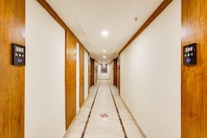 A hotel hallway with wooden paneling, numbered doors, and a marble floor with a star pattern. - Deluxealandur Near Chennai Airport (Chennai)