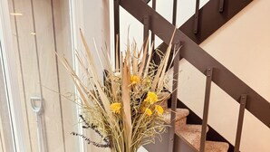 Una sala de estar con un sofá, un jarrón decorativo con plantas secas y una escalera al fondo.